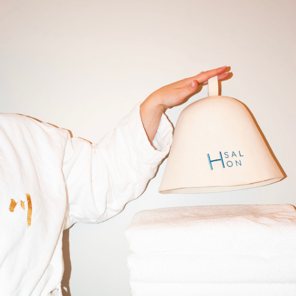 Person holding a H Salon sauna hat over white towels