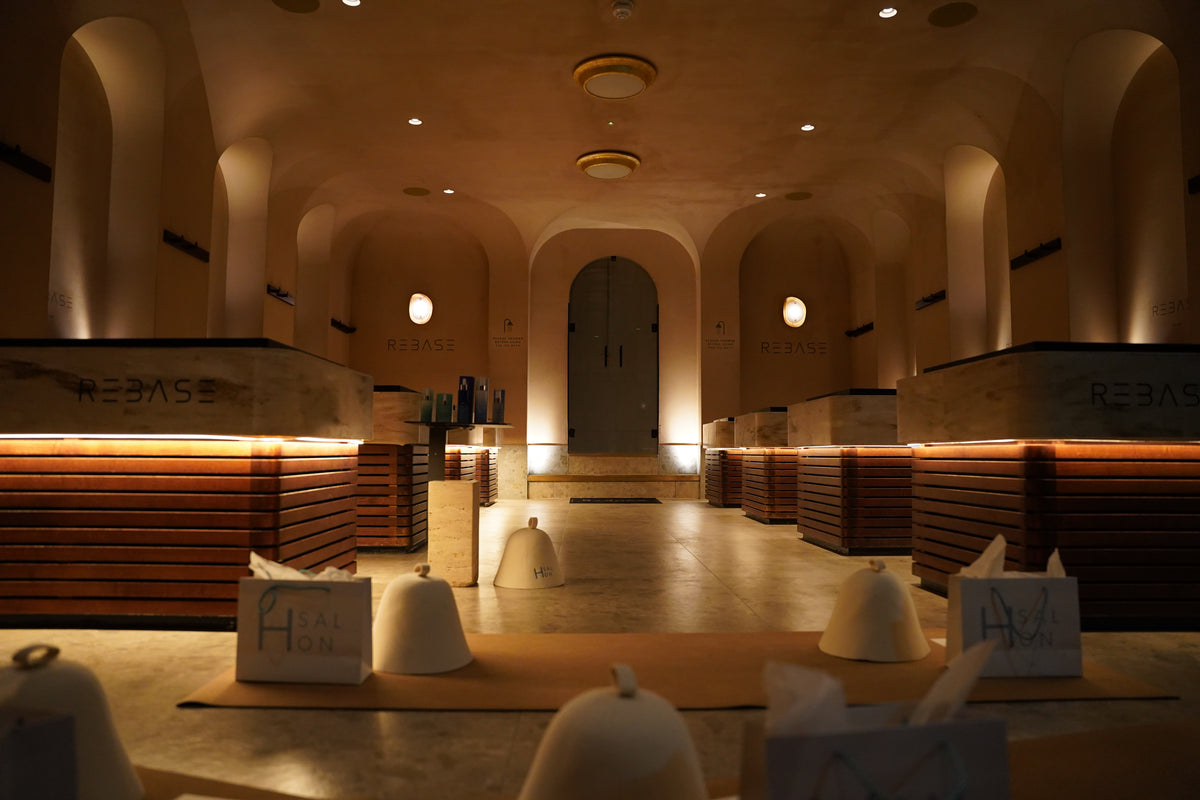 A dimly lit restaurant or lounge interior with arched walls, warm ambient lighting, wooden counter-like seating, and several white dome-shaped table covers or napkins placed on tables in the foreground.