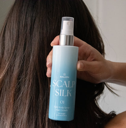 Person holding a bottle of  H Salon Scalp Silk spray with long hair in the background