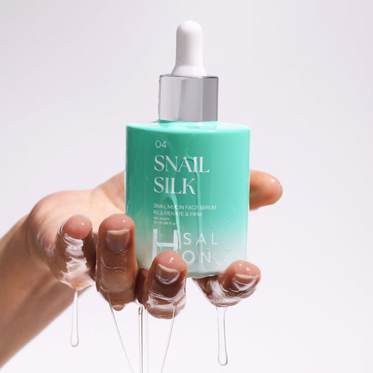 Hand holding a bottle of Snail Silk serum with a white background